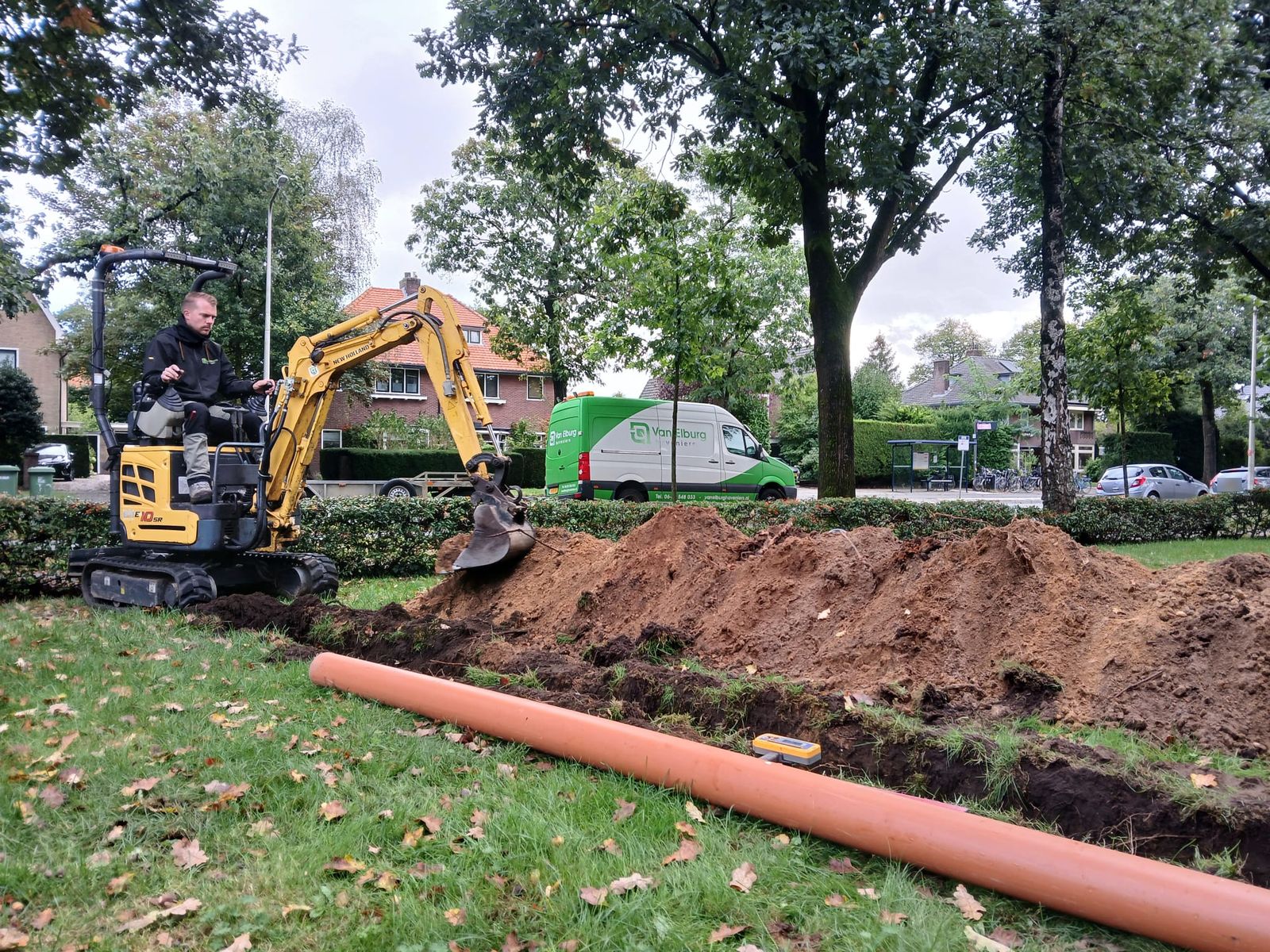 Nieuwe rioolleiding leggen met een minigraver in het gras